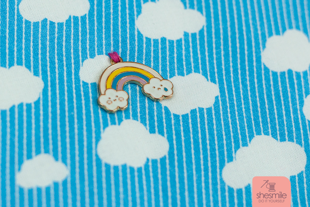Dadurch, dass der Außenstoff mit Bügelvlies H640 gestärkt bzw. gepolstert ist, konnte ich den Regenbogen Charm-Anhänger einfach mit dem Zick-Zack-Stich aufnähen. Den Transporter der Nähmaschine hab ich dafür ausgeschalten. Die überstehenden Fäden auf die Rückseite gezogen und von hinten verknotet.