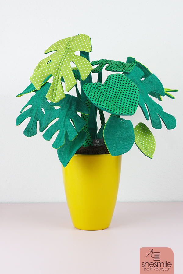 Eine Zimmerpflanze Frieda Flower, Version Monstera nähen. Eine Nähanleitung mit Schnittmuster von shesmile. Pflanzen aus Stoff. Perfekt für Allergiker, das Kinderzimmer, Vielreisende, kranke und alte Menschen, schattige Plätzchen oder einfach nur Pflanzendummies wie mich! Als Geschenk oder für sich selbst. Ein super Nähprojekt für die Stoffrestekiste und lässt sich an jede Blumentopfgröße ganz einfach anpassen. Diese Zimmerpflanzen muss man nicht gießen, umtopfen oder pflegen. Sie wachsen auch nicht über deinen Lieblingsblumentopf hinaus. Die Blätter werden nicht braun und kleine Fliegen in der Erde kannst du hier lange suchen. Klingt perfekt? Finde ich auch!