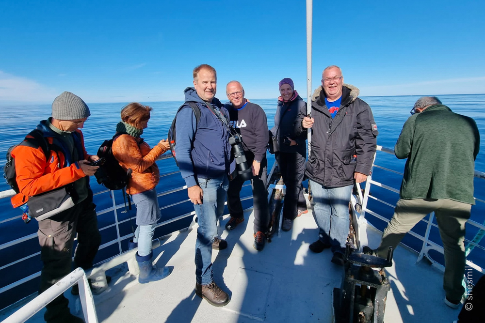 Neben mir ganz vorne oben auf dem Schiff drei Männer, die sich auf deutsch unterhalten haben. Einer davon, Michel Jürgensen, lebt wohl schon seit 30 Jahren hier in Norwegen. Eine Reportage dazu findet man auch unter www.ndr.de (Ab Minute 42). Die andern beiden (Gerhard und Jürgen) haben ihren Freund (nach einer längeren Corona-Pause) endlich mal wieder besucht. Sein Objektiv, ungefähr 4x so lang wie meines. Von ihnen und der Besatzung an Board habe ich dann erfahren, dass der Kapitän über das Sonar das Klicken des Pottwals abhört und relativ genau sagen kann, wann er auftaucht. Nämlich genau dann, wenn das Klicken aufhört. Klick-Geräusche macht der Pottwal nämlich nur in tieferen Gewässern, wo er nichts mehr sehen kann. Dann „hört“ er über das Echo der Klickgeräusche.