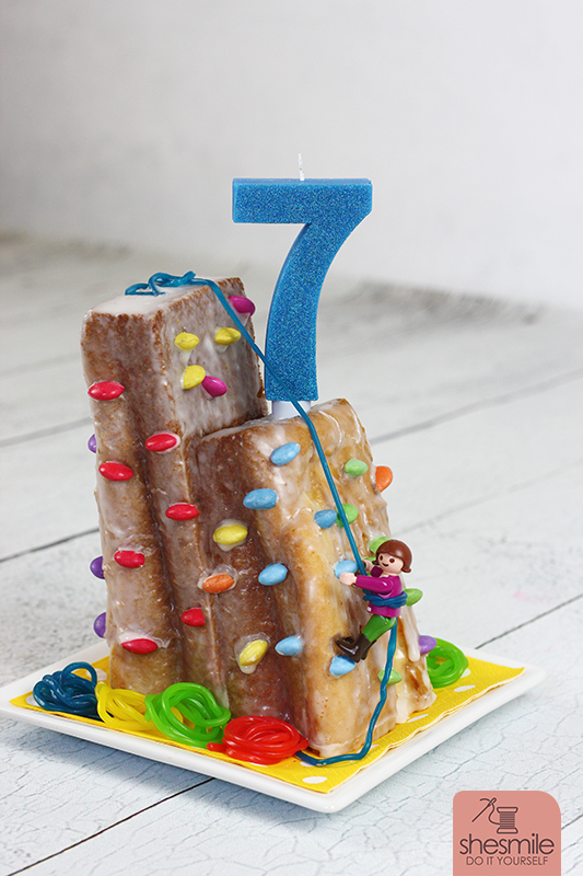 Ein Kletterwand-Kuchen zum siebten Kindergeburtstag in der Boulderhalle. Mit Smarties, Gummibärchen-Seilen und Playmobil-Figur. Gebacken und Dekoriert von shesmile.