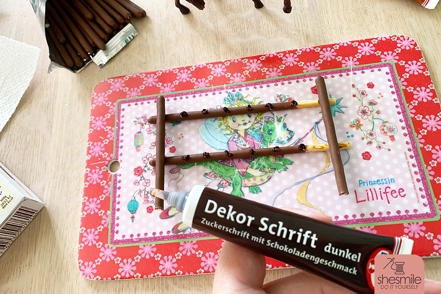 Einen Zaun aus Mikado-Stäbchen basteln. Geht ganz einfach mit Schoko-Zuckerschrift von Dr. Oetker. Eine Idee von shesmile.
