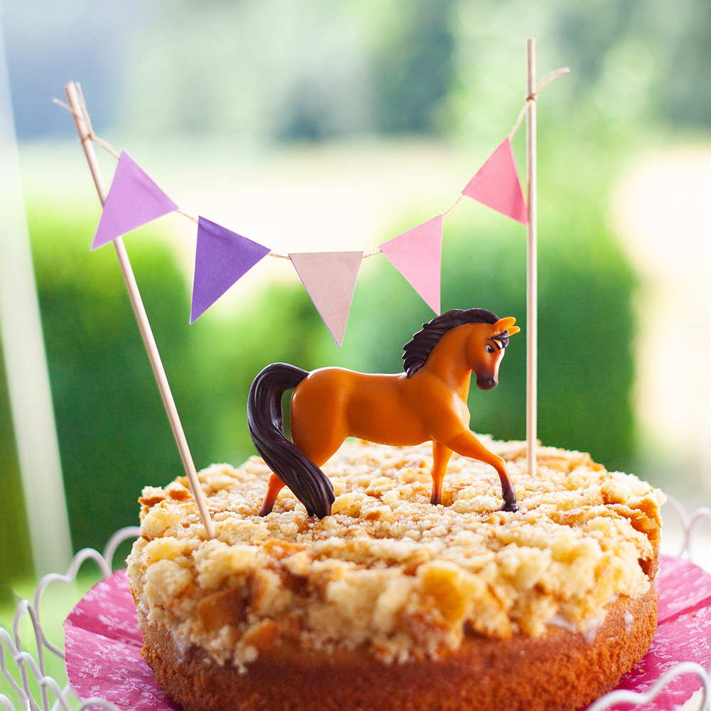 Pferdeparty im Garten mit dem passenden Kuchen: Pferdekoppel-Kuchen mit Wimpelkette und Spirit als Spielpferd und Kuchentopper. Eine Backidee von shesmile.