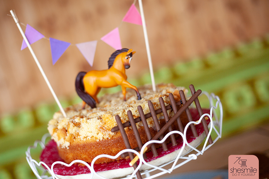 Pferdeparty im Garten mit dem passenden Kuchen: Pferdekoppel-Kuchen mit Wimpelkette und Spirit als Spielpferd und Kuchentopper. Eine Backidee von shesmile.