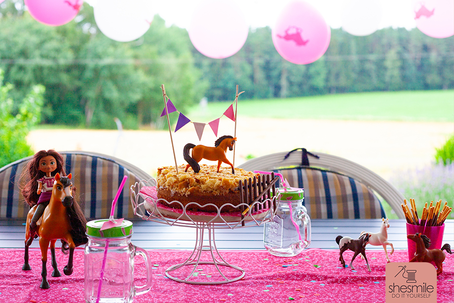 Pferdeparty im Garten mit dem passenden Kuchen: Pferdekoppel-Kuchen mit Wimpelkette und Spirit als Spielpferd und Kuchentopper. Eine Backidee von shesmile.