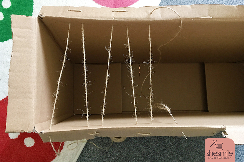 Danach nähst du mit einer dicken Stopfnadel und festem Nähgarn oder Paketschnur Begrenzungen in den Karton. Webe auf jeder Seite 2x durch den Karton und die umgefaltete Lasche so kann die Schnur nicht ausreißen.