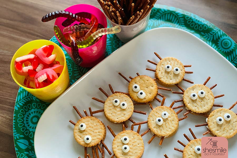 Alles was du brauchst sind Cracker-Kekse, Salzstangen, Augen und eine streichbare Creme. Damit erstellst du lustige Spinnen-Cracker für die Kinder-Halloween-Party. Eine Idee von shesmile.de