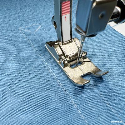 Den Taschenschlitz mit einem Lineal aufzeichnen und feststecken. Beide Stofflagen zusammennähen. Nahtlinie ist das Rechteck des Taschenschlitzes. Den Taschenschlitz mit einer spitzen Schere oder einem Skalpell einschneiden. Vorsichtig! Die Spitzen an den Enden bis knapp zur Naht einschneiden.