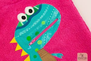 Ein Taschentier Dino mit Reißverschluss-Mund von Kleiner Polli-Klecks auf einem Frotteelo-Kulturbeutel aus Frottee von shesmile. Eine BuddieAktion von Die Ebookmacher.