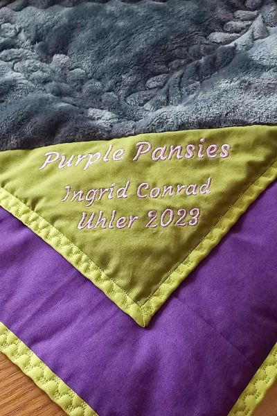 Ich nähe mein Binding bei den Patchworkdecken immer zuerst an der Rückseite fest, dann vorne mit einem breiteren Zierstich. So sieht man auch kleinere Abweichungen kaum. Der grüne Stoff ist die Rückseite, lila ist die Vorderseite.