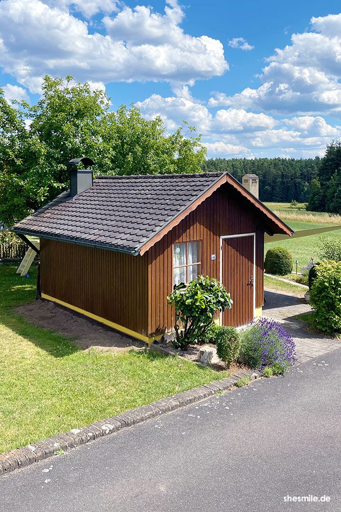 Die Idee zum Gartenhäuschen stammt von meiner Mama. ❤ Gebaut wurde es von der ortsansässigen Zimmerei Munker. Auf der Südseite sind zwei große Fenster welche über einen Rollo geöffnet werden können und dessen breite Fensterbretter zum Sitzen einladen. Im Inneren gibt es gemütliche Couchen, Liegestühle und einen Kaminofen mit Grillmöglichkeit. So viele Feste und Partys wurden in dem kleinen Holzhäuschen schon gefeiert. Ich möchte das Gartenhäuschen nicht mehr missen und hoffe, dass es durch den neuen Anstrich weitere 40 Jahre halten wird.