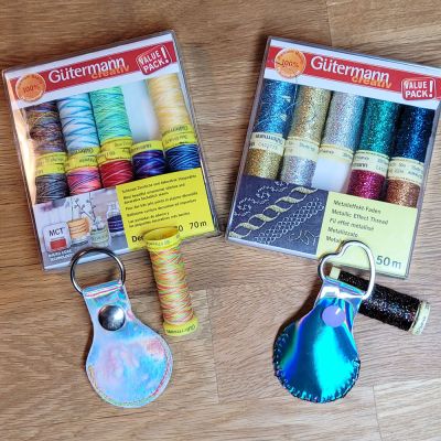 Bei dem ersten Anhänger (ganz in Silber) hab ich etwas schillernden Stoff auf die textile Seite geklebt. Da es noch (lt. Hersteller) festgebügelt werden musste, ging dies leider auf Kosten des schönen Glanzes ... mit dem Metalleffekt-Faden von Gütermann hatte meine Maschine Probleme (trotz Metallic-Nadel), so dass ich auf das Farbverlaufsgarn (Deco Stitch 70, Gütermann) wechselte. Den zweiten Anhänger (in Silber und Blau) hab ich mit einem 12,4 mm ColorSnap von Prym versehen und hab ihn dann per Hand mit Metallicgarn zusammengenäht.